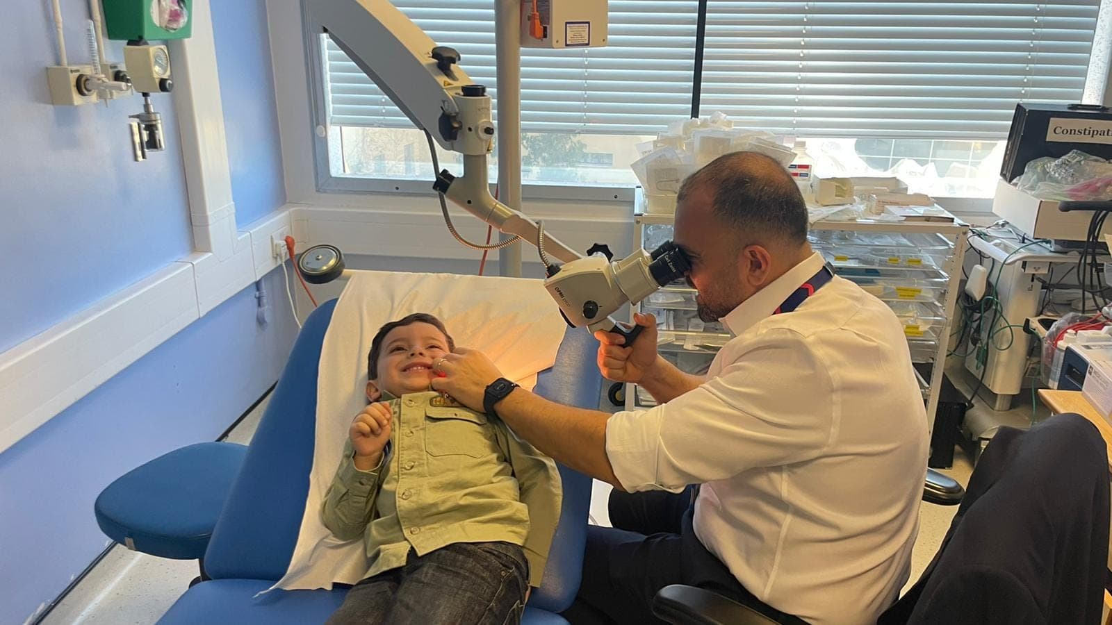 Mr Anwar examining a smiling young child's ear under the microscope